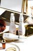 Travel-sized shampoo, conditioner and volumnizing mist on a vanity with gold accessories